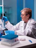 Senior chemist scientist doing experiment with blood in test tube. Researcher in medicine lab working with professional technology equipment for diagnostics development and healthcare. photo