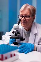 Senior scientist looking through microscope at sample in biology lab. Laboratory for scientific research with professional equipment for virus study and diagnosis biotechnolog development. photo