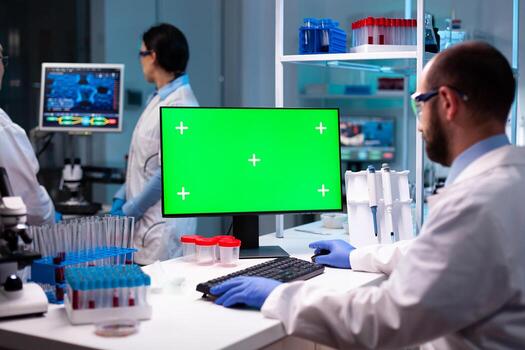 Biochemist working in laboratory using green mock-up screen chroma key.Team of microbiologists doing vaccine analysis and discovery treatment cure against covid19. photo