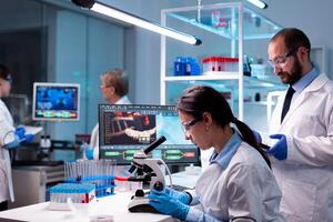 Woman scientist analyzing virus with microscope in research chemistry lab with team. Doctor and chemists examening vaccine evolution, working at diagnosis development. photo