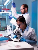 Scientist looking at blood sample through microscop and assitant taking liquid with micropipette. Modern lab for scientific research with professional equipment for vaccine development diagnosing virus evolution. photo