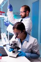Scientist taking sample with micropipette from test tube and asistant analyzing virus on blood through microscop. Modern lab for scientific research with professional equipment for vaccine development diagnosing virus evolution. photo