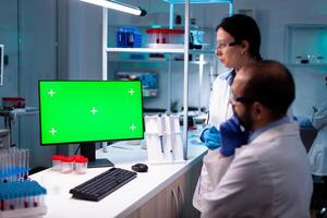 Modern medical research laboratory with two scientists using computer with green chroma key screen. Doctors specialists discovering scientifc experiment with technology equipment industry. photo
