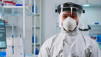 Portrait of scientist man wearing coverall smiling at camera sitting in modern equipped laboratory. Chemist doctor xamining virus evolution using high tech for scientific research, vaccine development photo