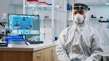 Portrait of experienced scientist man in coverall smiling at camera wearing protection mask in equipped lab. Examining virus evolution using high tech and chemistry tools for vaccine development. photo