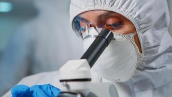 Portrait of lab technician with protection suit examining samples using microscope in equipped laboratory. Scientist working with various bacteria, tissue and blood samples for pharmaceutical research photo