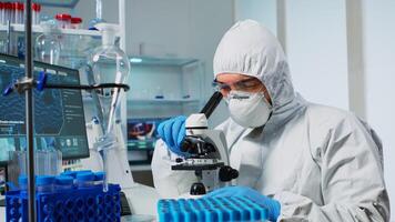 Medical research scientist in ppe suit conducting vaccine development using digital microscope in a biological applied science laboratory. Caucasian lab engineer in coverall working on medical treatment photo