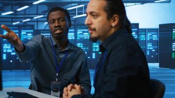 Upbeat african american computer scientist and coworker upgrading equipment in data center. Joyous admin at PC desk in high tech facility overseeing server clusters helped by colleague photo