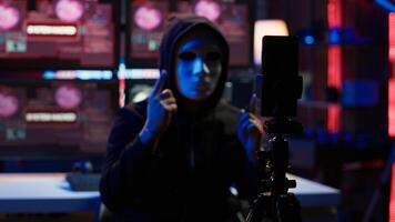 Focus on camera on phone on tripod used by hacker concealing identity filming ransom in hidden base. Close up of smartphone used by cybercriminal with mask to record blackmail footage, camera A photo