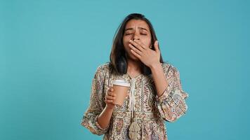 Woman suffering from insomnia yawning, sipping coffee to gain energy and get rid of pain. Tired person feeling drowsy after sleepless night, drinking caffeinated beverage, studio background, camera A photo