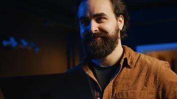 Happy man doing IT support job from home, standing in personal office with laptop in hand, coding, close up. Cheerful programmer writing lines of code on notebook in living room photo