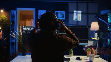 Engineer wearing headphones while using coding to fortify security, remotely working for IT company. Software expert listening music and upgrading binary code scripts on computer, camera B photo