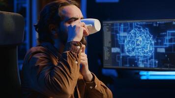 Computer scientist updating artificial intelligence neural networks, drinking coffee and writing code scripts in personal office. IT expert enjoying hot beverage while running AI simulations, camera A photo