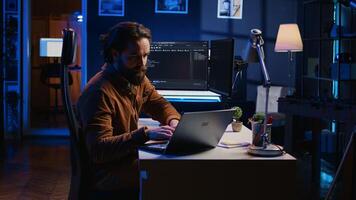 Computer scientist putting headphones on while developing code on PC, making time pass faster during remote job shift. IT admin doing multitasking in home office while listening music, camera B photo