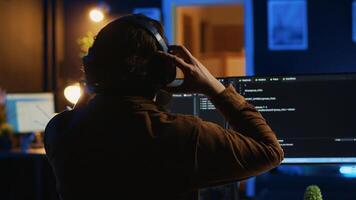 Engineer wearing headphones while using coding to fortify security, remotely working for IT company. Software expert listening music and upgrading binary code scripts on computer, camera A photo