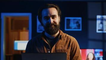 Portrait of happy man doing IT support job from apartment, standing in personal office with laptop in hand, coding. Joyful developer writing lines of code on notebook, camera A close up shot photo