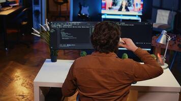 Computer scientist at home office desk writes binary code scripts and drinks from mug of coffee. IT expert in apartment enjoying tea while using programming to safeguard consumer data, camera B photo