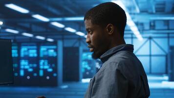 African american man working in server hub capable of processing vast amounts of data. IT programmer at PC desk typing on keyboard, updating servers controlling network resources, close up shot photo