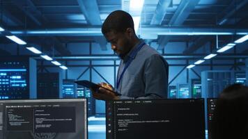 Manager uses tablet, supervising team programming servers providing computing resources for different workloads. Inspector using device to oversee engineers in data center mending supercomputers photo