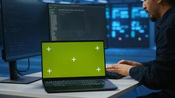 Isolated screen notebook in front of employee working in server farm used for processing data. Close up shot of mockup laptop on desk next to IT developer typing at PC, updating servers photo