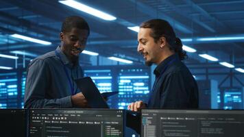 Coworking system administrators in server hub monitoring data center energy consumption across hardware using tablet. Colleagues inspecting supercomputers, ensuring malfunctions are fixed photo