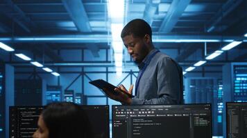 Engineer inputting data on tablet in server hub, monitoring data center energy consumption across hardware. Technician inspecting mainframes, ensuring malfunctions are repaired photo