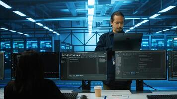 Smiling admin doing yearly checkup to prolong data center electronics life span and avoid downtime. Upbeat employee in server room monitoring server infrastructure components using laptop photo