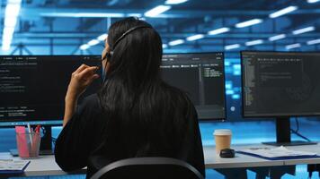 Computer scientist upgrading equipment in data center, wearing headphones to listen music. Programmer at PC desk in high tech establishment overseeing server rows, typing on keyboard photo