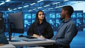 Multiracial team of IT engineers in server room brainstorming ways to fix equipment storing datasets. Indian and african american coworkers discussing how to mend racks doing computational operations photo