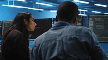 Diverse IT engineers in server room brainstorming ways to fix equipment storing datasets. Multiethnic coworkers discussing how to mend data center racks doing complex computational operations photo