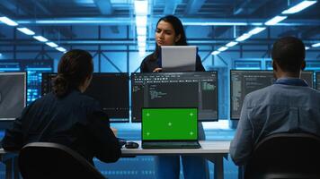 Multiethnic engineers working in high tech server hub, using green screen laptop and PCs to analyze data. Diverse employees examining infrastructure in data center, using chroma key notebook photo