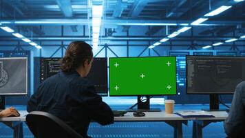 IT support workers in data center coding on green screen computers, upgrading equipment. Multiethnic team of engineers at PC desk overseeing server clusters using mockup monitors photo
