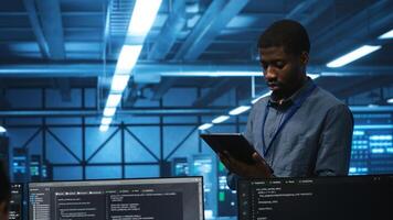 Technician in server hub using tablet to find hardware misconfigurations affecting rackmounts performance. Man checking data center infrastructure devices bottlenecks leading to errors photo