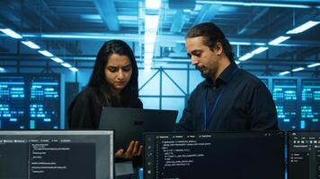 Technicians working in high tech server hub, analyzing data on laptop to ensure seamless data flow. Coworkers examining equipment in data center, ensuring system integrity and security photo