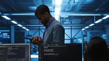 Technician doing system analysis using tablet, doing needed adjustments in supercomputers server farm. Engineer overseeing data center housing storage infrastructure supporting critical IT workloads photo