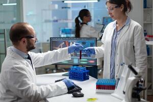 Microbiology team working at biochemistry experiment analyzing blood test tube in hospital laboratory. Scientists investigating dna sample discussing biomedical treatment. Sickness investigation photo