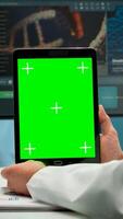 Close up of biochemist sitting at workplace in laboratory using green mock-up screen tablet with chroma key display while coworker working in background bringing blood sample. photo