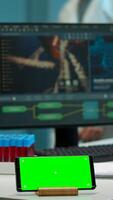 Microbiologist bringing blood samples in modern lab putting them near smartphone working with green chroma key screen placed on desk. Team of biotechnology scientists developing drugs in background photo