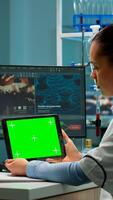 Scientist holding tablet with green mockup, looking on device with chroma key, isolated display. Microbiologists doing virus research, in background man lab researcher working at vaccine developent. photo