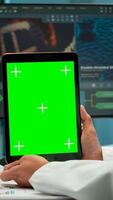 Male chemist scientist holding green mock-up screen tablet sitting at desk. In background technology research, development laboratory with specialist doctor working in high tech design photo