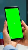 Close up of doctor's hand holding phone with green screen sitting at desk in biological laboratory while nurse bringing blood samples. Scientist using smartphone with mockup, chroma key display photo