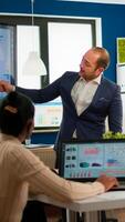 Business partner presenting company strategy to diverse team brainstorming in new startup office, analysing financial graphs from display, Multiethnical businesspeople working in professional start up photo