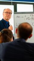 Confident man business coach giving flipchart presentation training diverse workers group at workshop, businessman presenter leader mentor explaining graph teaching team employees at corporate meeting photo