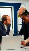 Diverse businesspeople working in teamwork discussing project strategy using laptop standing at conference table. Manager executive analysing financial data during business meeting in broadroom photo