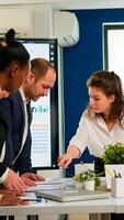 Diverse team of workers talking, looking at documents and analyzing graphs data standing at conference desk in start up company. Professional colleagues team discussing marketing project brainstorming photo