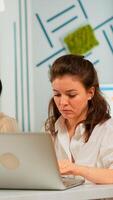 Focused woman manager typing on laptop, browsing on internet while sitting at desk concentrated having multitasks. Multiethnic coworkers talking about startup financial company in modern office. photo