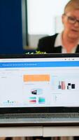 Busy multicultural diverse employees analysing annual financial statistics sitting at conference desk in back of laptop holding documents searching business solutions. Business team working in company photo