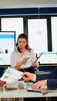 Team leader explain to multiracial workmates new project standing at desk in broadroom, holding clipboard. Corporate staff discussing new business application with colleagues looking at screen photo