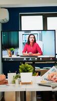 Manager woman sitting in front of camera talking on call during virtual conference working in business modern office. Diverse team planning strategy during conference, online brainstorming photo