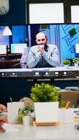 Manager man talking with colleague using call for virtual meeting, employees sitting in broadroom looking tv screen. Diverse team planning strategy during conference, online brainstorming photo